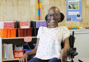 A Black woman sits in a wheelchair inside a classroom