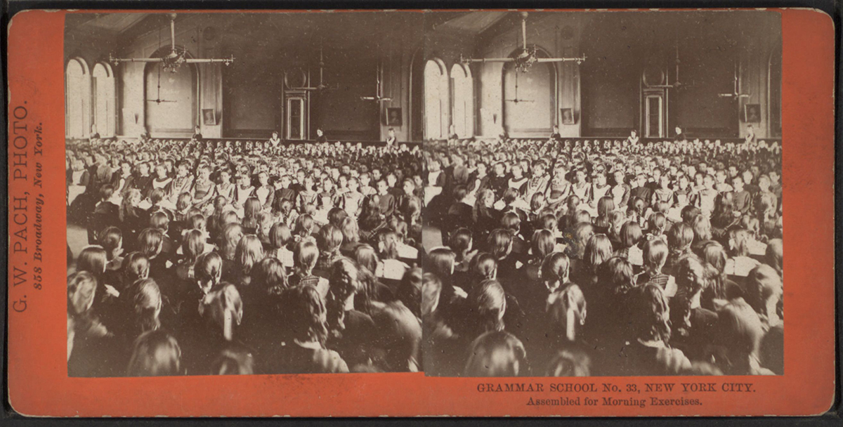 A stereoscopic slide with photos taken from two slightly different angles shows around 100 schoolgirls seated in a large auditorium with several women teachers in the background.